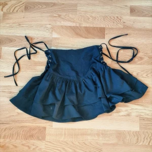 Svart volangkjol med snörning - Supersnygg svart kjol med volanger och snörningsdetaljer i sidorna. Kjolen är högmidjad men har en drop-waist känsla. Dragkedja finns baktill men snörningen kan man även dra åt på sidorna för att få en mer "snatched" look.