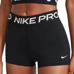 Svarta träningstights shorts från Nike - Svarta tighta träningstights shorts från Nike med vit logga på benet och bred resår i midjan med texten 'NIKE PRO'. Perfekta för gym, löpning eller annan träning.