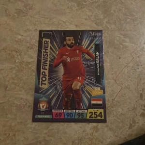 Premier League samlarkort Mohamed Salah - Säljer ett Premier League samlarkort med Mohamed Salah från Liverpool FC. Kortet har färgstark design med texten 'Top Finisher' och visar Salah i röd matchdräkt. Kortet har statistik som Defence 69, Control 90 och Attack 95.