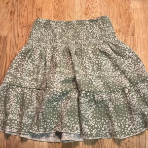 Grön mönstrad kjol från Gina Tricot - Supersöt grön kjol från Gina Tricot i storlek XS. Kjolen har vitt prickigt mönster, smock i midjan och volangdetaljer🫶💞