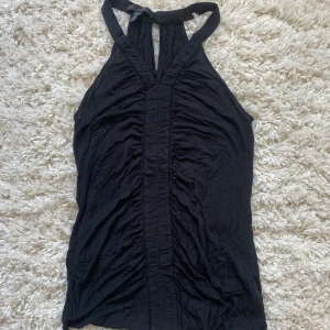Svart halterneck topp från Kenneth Cole - Säljer en svart halterneck topp från Kenneth Cole. Toppen har en snygg detalj med veck framtill och en liten öppning vid halsen. Perfekt till varma dagar eller som ett statement-plagg. Används tyvärr inte längre💗