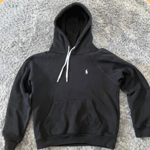 Svart hoodie från Ralph Lauren - Svart hoodie från Ralph Lauren med vita snören. Perfekt för en avslappnad stil.