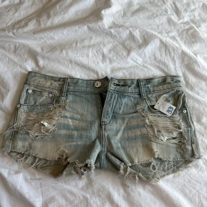 Ljusblå slitna jeansshorts från Energy Denim - Ljusblå jeansshorts med slitna detaljer och fransar från Energy Denim. Klassisk femficksmodell med låg midja och råa kanter. Perfekta för sommaren och ger en cool, avslappnad look.