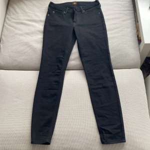 Svarta skinny jeans från Lee - Säljer ett par svarta skinny jeans från Lee med klassisk femficksdesign och diskreta detaljer. Jeansen har normalhög midja och smal passform hela vägen ner. Perfekta till många olika stilar och enkla att matcha. (För små för mig)
