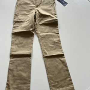 Beiga chinos från Polo Ralph Lauren - Snygga beiga chinos från Polo Ralph Lauren i klassisk modell. Byxorna har normal passform med raka ben och är tillverkade i bomull. Perfekta för en stilren look och passar till många olika tillfällen. För barn