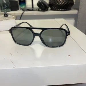 Svarta solglasögon  - Snygga svarta solglasögon med en klassisk design och mörk gröna linser. De har en robust ram och en stilren look som passar perfekt för soliga dagar. Perfekt accessoar för att komplettera din outfit.