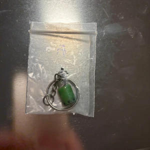 Nyckelring med grön pärla - En unik nyckelring med en grön pärla i glas. Den har en metallkedja och en ring för att fästa nycklar. Perfekt som en liten accessoar för att ge nyckelknippan en personlig touch.