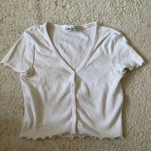Vit T-shirt med knappar - Säljer en söt vit ribbad topp med korta ärmar och v-ringning i storlek M