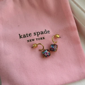Kate Spade örhängen - Jättefina örhängen från Kate Spade New York. De är guldfärgade och är glittriga i flera färger. Creoler med ett hängsmycke. Baktill finns Kate Spade märket instämplat samt en sten. Aldrig använda och därav i mycket fint skick!💕Fick i present så har tyvärr inget kvitto. Påsen på första bilden medföljer. Hör gärna av dig vid frågor eller funderingar
