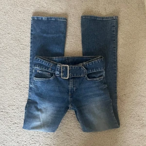 Blå jeans med bälte - Snygga blå jeans med ett skärp som går att ta av. Bootcut, lågmidjade. Midjemått: 37cm innerbenslängd: 75cm