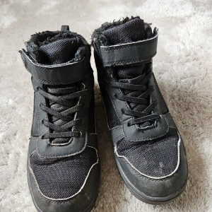 Svarta sneakers från Take Off - Snygga svarta sneakers från Take Off med snörning och kardborreband. Skorna har en robust design med rund tå och är perfekta för vardagsbruk. De är tillverkade i syntetmaterial och har en bekväm passform.