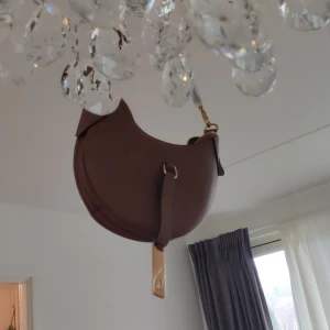 Ralph Lauren, Brun axelväska med dragkedja - Snygg brun axelväska i skinn med guldfärgade detaljer och dragkedja upptill. Väskan har en justerbar axelrem och en stilren design som passar perfekt för alla tillfällen.