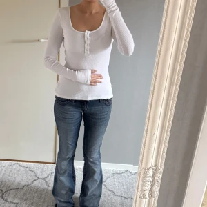 Vit ribbad topp från Nelly - Säljer en stilren vit ribbad topp från Nelly med lång ärm och knappar framtill.  Använd några gånger men är fortfarande i fint skick!