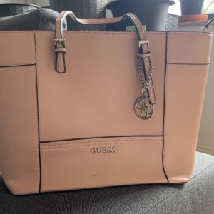 Rosa väska från Guess - Säljer väska från Guess, som man ser på kanten längst upp är den lite sliten. Många fack i och man får plats med mycket🫶🏻