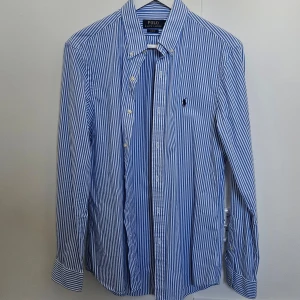 Blåvit randig skjorta från Polo Ralph Lauren - Snygg blåvit randig skjorta från Polo Ralph Lauren i slim fit storlek M. Skjortan har långa ärmar och knappar framtill. Den är broderad med den klassiska logotypen på bröstet. Passar perfekt till sommaren! Den är knappt använd och passade inte mig så därför nytt skick. Nypris ligger på 1800kr