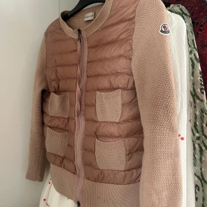 Moncler cardigan/jacka  - Säljer en moncler cardigan i rosa/beige färg. (Den är lite mer rosa än på bilden) i storlek M men skulle säga att den passar en Xs. Scan finns i jackan💕 (jackan är lite smutsig men det går o tvätta enkelt) , pyttelitet hål vid nacken men inget man ser.💕