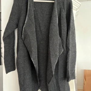 Grå kofta från Wera Stockholm - Säljer en stilren grå kofta från Wera Stockholm. Koftan har en öppen design utan knappar och är perfekt för lager-på-lager. Den är långärmad och tillverkad i ett mjukt material som passar bra för kyligare dagar.