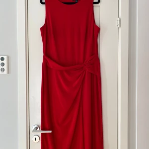 Röd ärmlös klänning från Ralph Lauren - Snygg röd klänning från Ralph Lauren med en elegant knytdetalj i midjan. Klänningen är ärmlös och har en klassisk, tidlös design som passar perfekt för speciella tillfällen.                                                         Röd armlös klänning i strl 12 (42) från Ralph Lauren.  Endast använd en gång och i nyskick.  Mått Över bröstet: ca 51 cm Längd från axeln och ner: ca 119 cm  95% polyester och 5% elastan  Kommer från ett djur och rökfritt hem. 