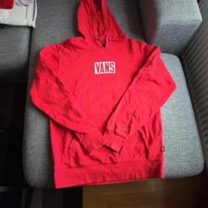 Röd hoodie från Vans - Säljer en cool röd hoodie från Vans med deras ikoniska logga på bröstet och stort tryck på ryggen. Perfekt för en avslappnad stil. Hoodien har en klassisk passform med långa ärmar och en bekväm huva.