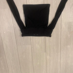 Svart ribbad topp från Stradivarius - Säljer en svart ribbad topp från Stradivarius. Toppen har en stilren design med långa ärmar och en åtsittande passform. Perfekt för att matcha med olika outfits. Hör av dig vid intresse!