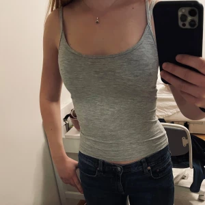 Grå linnetopp - Säljer en grå linnetopp med smala axelband. Perfekt för varma dagar eller som ett lager under andra plagg. Toppen har en tight passform som framhäver figuren. Fin urringning bak. 
