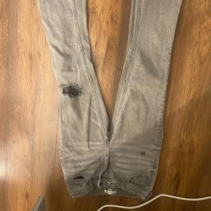 Grå jeansbyxor från Gina Tricot - Snygga grå jeansbyxor från Gina Tricot med en cool slitning på ena benet. Perfekta för en avslappnad stil. Byxorna har en klassisk femficksdesign och är tillverkade i ett bekvämt material.