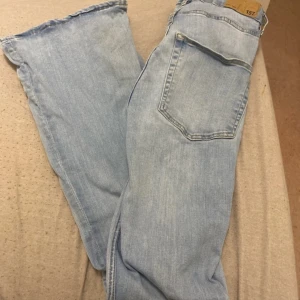 Ljusblå jeans med flare - Säljer ett par ljusblå jeans från lager med en snygg flare-stil. De har en klassisk femficksdesign och knappgylf. Perfekta för en avslappnad look.
