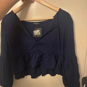 Mörkblå blus från Missay - Säljer en mörkblå blus från Missay med volangdetaljer. Blusen har en v-ringad design och långa ärmar. Perfekt för en stilren look.