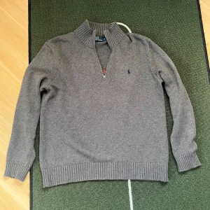Grå tröja med dragkedja från Polo Ralph Lauren - Säljer en stilren grå tröja från Polo Ralph Lauren med dragkedja och ribbad krage. En nice tröja i väldigt bra kvalité 