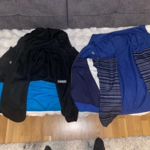 Svart och blå vindjacka från Lacoste - Säljer en snygg svart och blå vindjacka från Lacoste. Jackan har dragkedja och långa ärmar med randigt mönster. Perfekt för sportiga aktiviteter och har en cool design med vita detaljer.
