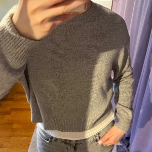 Grå stickad tröja - Säljer en stilren grå stickad tröja med rund hals och långa ärmar. lätt att matcha med olika outfits. Tröjan har en avslappnad passform och ribbade muddar vid ärmslut och nederkant.