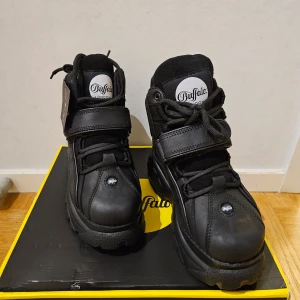 Svarta boots från Buffalo - Säljer ett par svarta boots från Buffalo med hög platåsula och snörning. Skorna har en robust design med kardborreband för extra stöd. Perfekta för en edgy look.