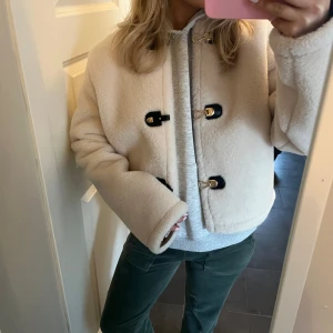 Beige teddyjacka med knappar - Säljer en superfin beige jacka från Zara. Jackan har en croppad passform och stängs med snygga svarta knappar. Perfekt för att hålla sig varm och stilren under kyligare dagar. Använd ish 2 gånger🥰 och säljer då jag har för många jackor!