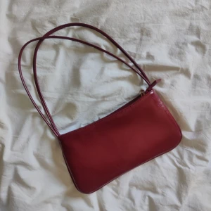Röd axelväska i skinn - Snygg röd axelväska i fakeskinn med en minimalistisk design. Väskan har en dragkedja upptill och dubbla axelremmar för enkel bärning. Perfekt för att ge en färgklick till din outfit.