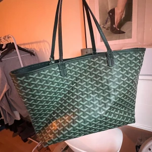 Grön handväska  - Snygg grön handväska med ett ikoniskt mönster. Väskan har långa handtag och är perfekt för att bära med sig allt man behöver. Den har en stilren design som passar till många olika tillfällen.