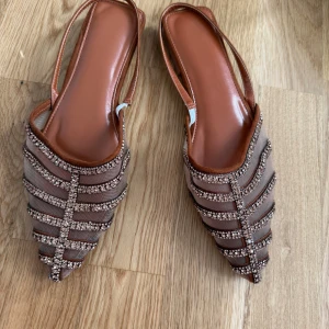 Bruna sandaler med glittriga detaljer - Snygga bruna sandaler med spetsig tå och glittriga detaljer. De har en öppen design med remmar och en elegant look. Perfekta för att ge en touch av glamour till din outfit.
