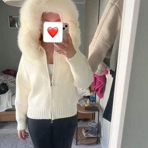 Vit jacka med pälshuva - Säljer en stilren vit jacka med en fluffig pälshuva. Jackan har dragkedja framtill och långa ärmar med ribbade muddar. Perfekt inför våren, den är ifrån alessa och är använd 1 gång!
