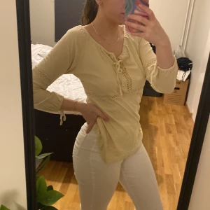 Beige långärmad topp med spetsdetaljer - Säljer en beige/krämvit långärmad vintage topp med fina spetsdetaljer och knytning framtill. Perfekt för en stilren look. Passar bra till både jeans och kjol. 
