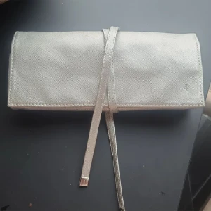 Edblad kuvertväska  - Kuvertväska för tex smycken eller smink från Edblad i skimrande silver. Många fack för förvaring med bland annat dragkedja och knappar. Väldigt praktisk och tar minimalt med plats. Nypris 499kr, aldrig använd.