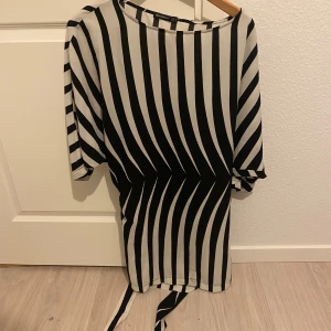 Svartvit randig klänning från Atmosphere - Säljer en stilren svartvit randig klänning från Atmosphere. Klänningen har trekvartsärmar och ett knytband i midjan för en snygg passform. Perfekt för en chic look!
