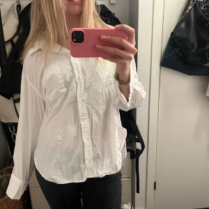 Vit skjorta - Säljer en klassisk vit skjorta med knappar framtill. Skjortan har en avslappnad passform och långa ärmar. Perfekt för en stilren look.