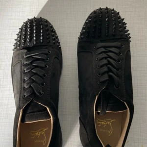 Christian louboutin sneaker svart - Helt nya snygga svarta sneakers från Christian Louboutin med coola nitar på tån och klassisk röd sula. Skorna har snörning och är tillverkade i skinn, vilket ger en lyxig känsla. Perfekta för att ge din outfit en edgy touch. Pris kan diskuteras!