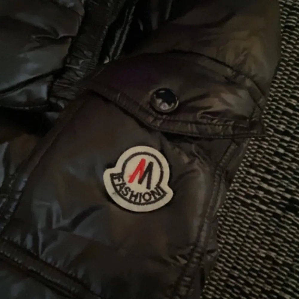 Snygg svart pufferjacka från M Fashion med dragkedja och knappar. Jackan har en huva och långa ärmar, perfekt för kyliga dagar. Den quiltade designen ger en modern look. Ett måste för garderoben!. Takit.
