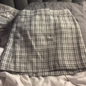 Rutig kortkjol från H&M, storlek 36 - Snygg kortkjol från H&M i svartvitt rutigt mönster. Kjolen har en klassisk A-linjeform och är tillverkad i ett tjockare tyg som ger en trendig och stilren look. Perfekt att matcha med boots eller en stickad tröja för en cool vibe.
