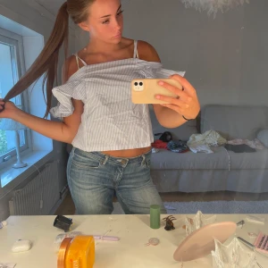 Randig offshoulder blus med volang - Säljer en ljusblå och vit randig blus med offshoulder och smala axelband. Toppen är croppad och har en snygg volangdetalj längs ärmarna. Perfekt för dig som gillar en chill och trendig stil på sommaren.