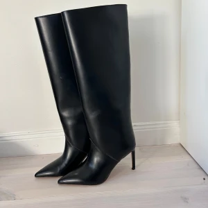 Svarta höga stövlar med klack - Snygga svarta stövlar med spetsig tå och hög klack. Stövlarna är tillverkade i slätt skinn och har en elegant, minimalistisk design. Helt nya, har aldrig använts