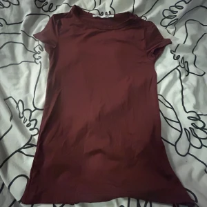 Vinröd kortärmad topp från 157 XS - En enkel och stilren vinröd topp från 157 i storlek XS. Modellen är kortärmad med rund hals och har en tight passform. Materialet känns mjukt och stretchigt, perfekt för att matcha med jeans eller kjol. Snygg att ha som basplagg i garderoben.