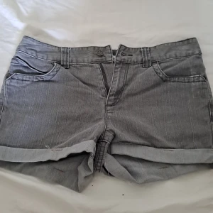 Gråa basic jeansshorts - Fina jeansshorts som är lite längre. Randiga detaljer och med blommor på bakfickorna. Köpt från en marknad i Thailand.