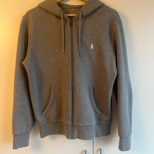 Grå hoodie från Polo Ralph Lauren - Jag säljer en polo Ralph lauren zip då den har blivit för liten. Skicket är bra men har en liten skada på ena armen. Den passar till mycket och är true size. Storleken är S. Priset går att diskutera. Ny pris 2200