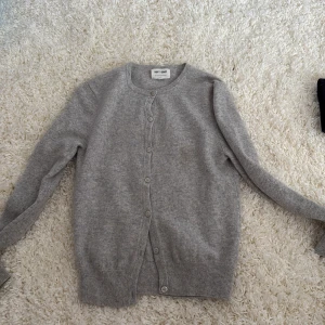 Grå kashmirkofta från Soft Goat XS - Snygg grå kofta i mjuk kashmir från Soft Goat, storlek XS. Klassisk rund hals, knappar framtill och ribbade muddar. Perfekt att slänga över en t-shirt för en chill look. Långärmad och i en neutral ljusgrå ton som passar till allt. OBS, en liten brun fläck som inte syns särkligt mycket men som är med på bilderna, kontakta vid frågor och funderingar!! Säljs ej längre på hemsidan. Pris kan diskuteras!